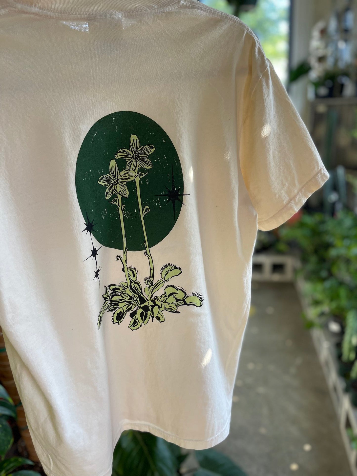 a beige colored t-shirt with with an illustration of a flytrap on the back of it