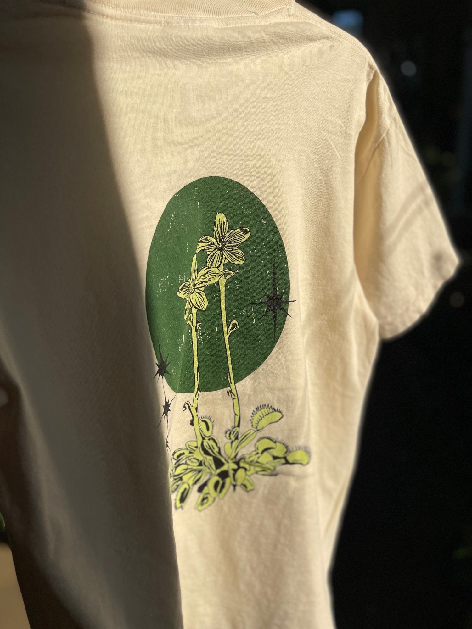 closeup of a beige colored shirt with an illustrated flytrap plant on the back of it